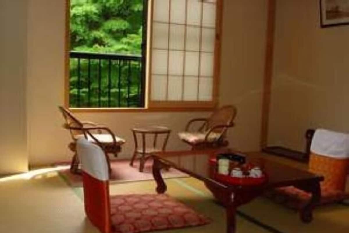A traditional Japanese-style room with tatami flooring, a low table, and a view of greenery outside.