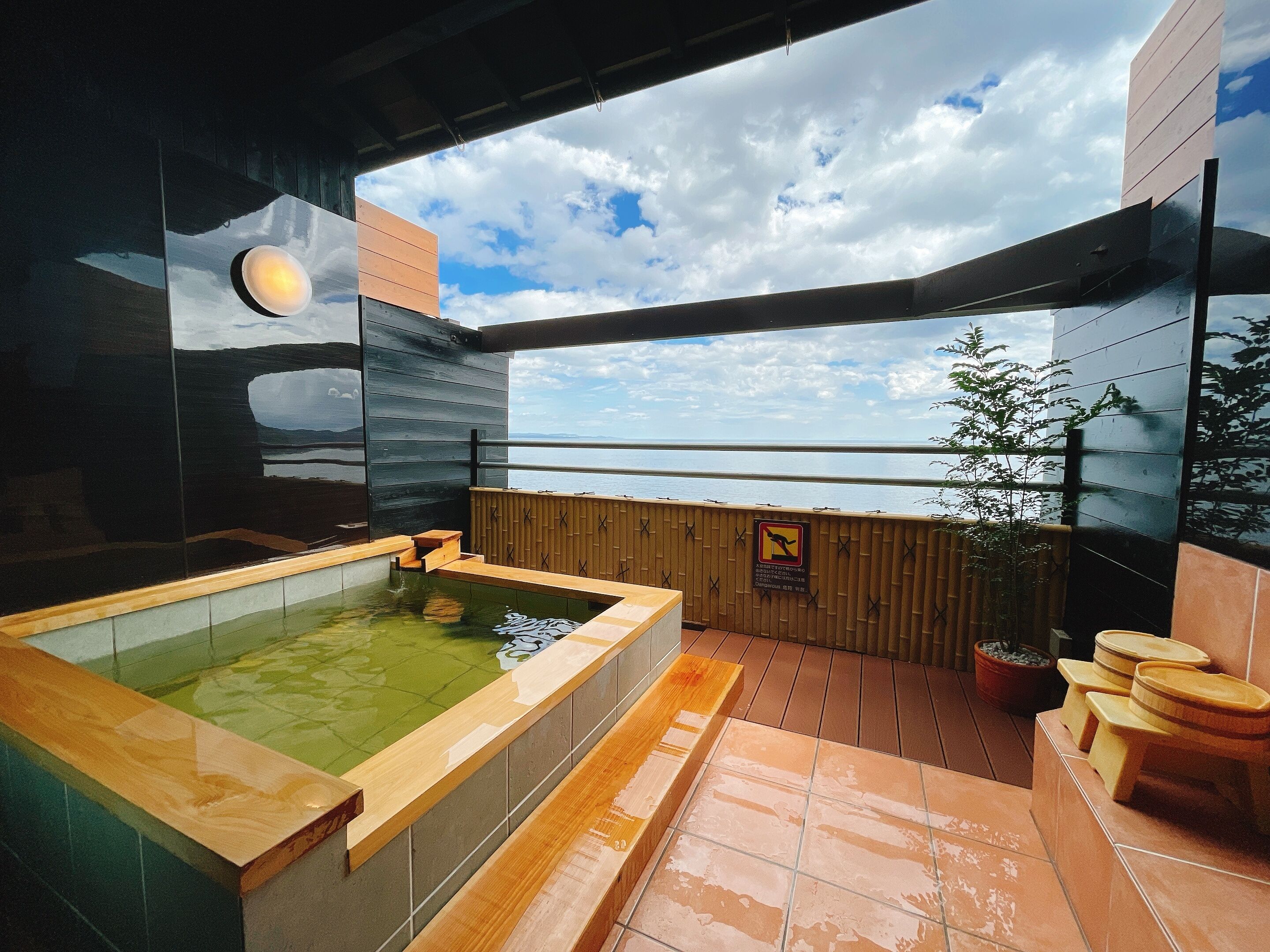 A modern spa with a large hot tub, wooden deck, and a view of the sea.