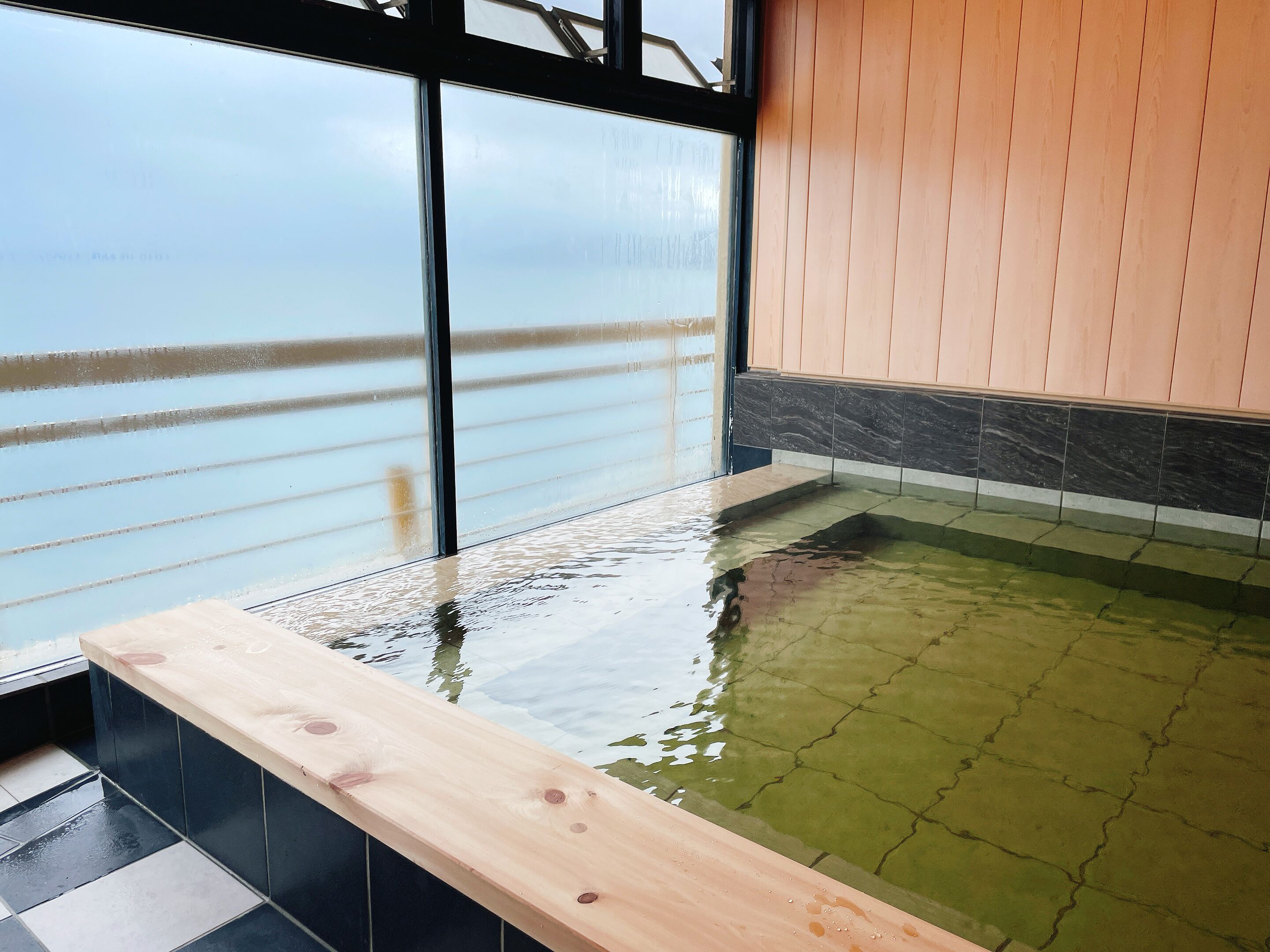 Una terraza de madera con piscina, vista al mar y suelo de baldosas.
