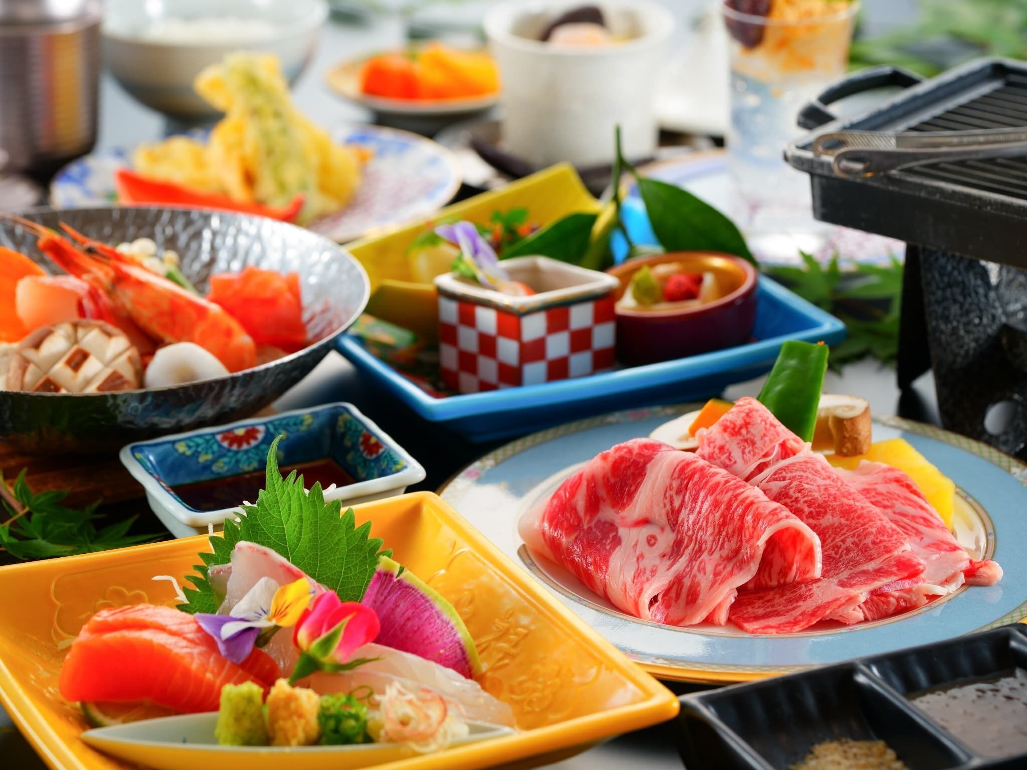 A variety of Japanese dishes including sushi, sashimi, and grilled meats, presented on a table with a grill in the background.