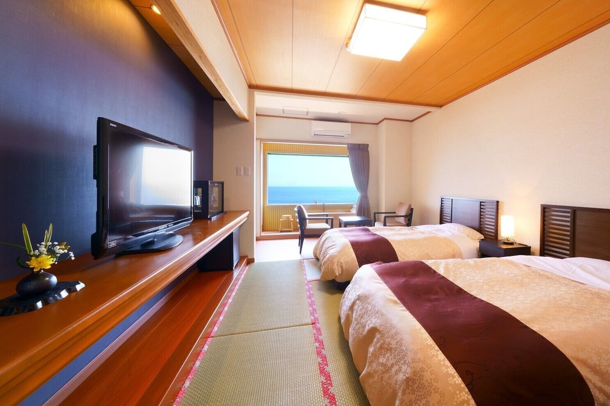 A hotel room with two beds, a television, a small table, and a view of the sea.
