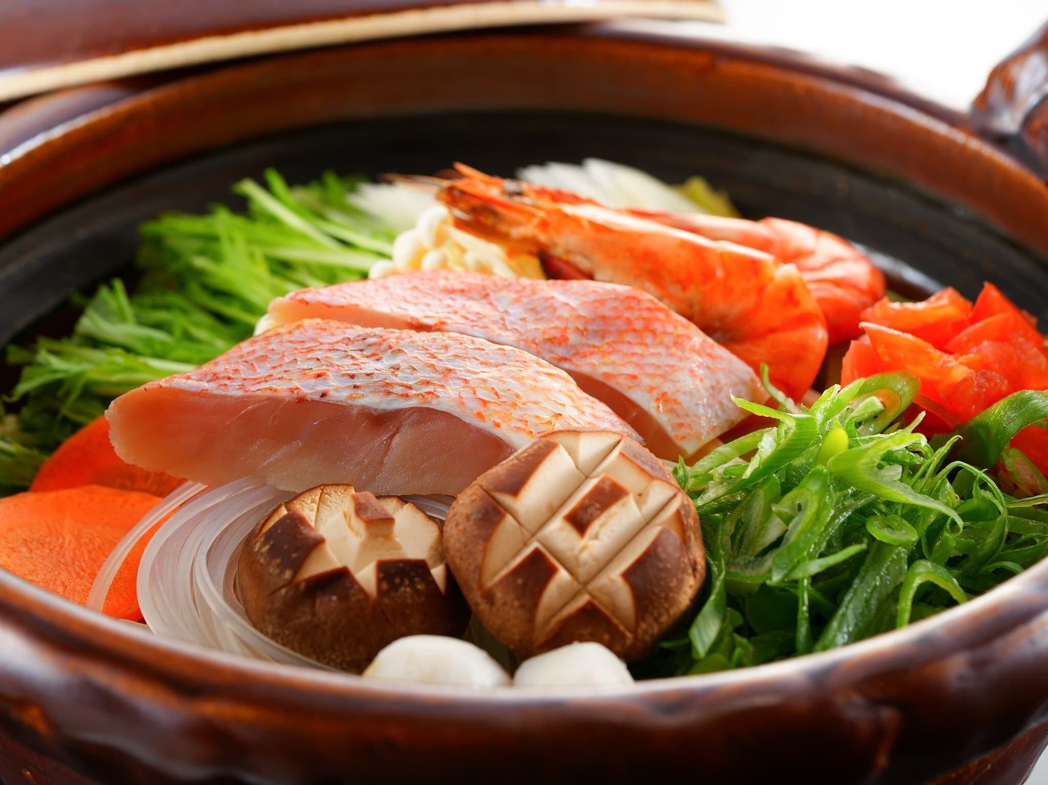 A hot pot with various ingredients including fish, vegetables, and mushrooms.