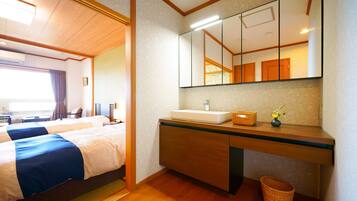 Habitación de hotel con dos camas, un tocador de madera con espejo, un lavabo y una pequeña cesta.