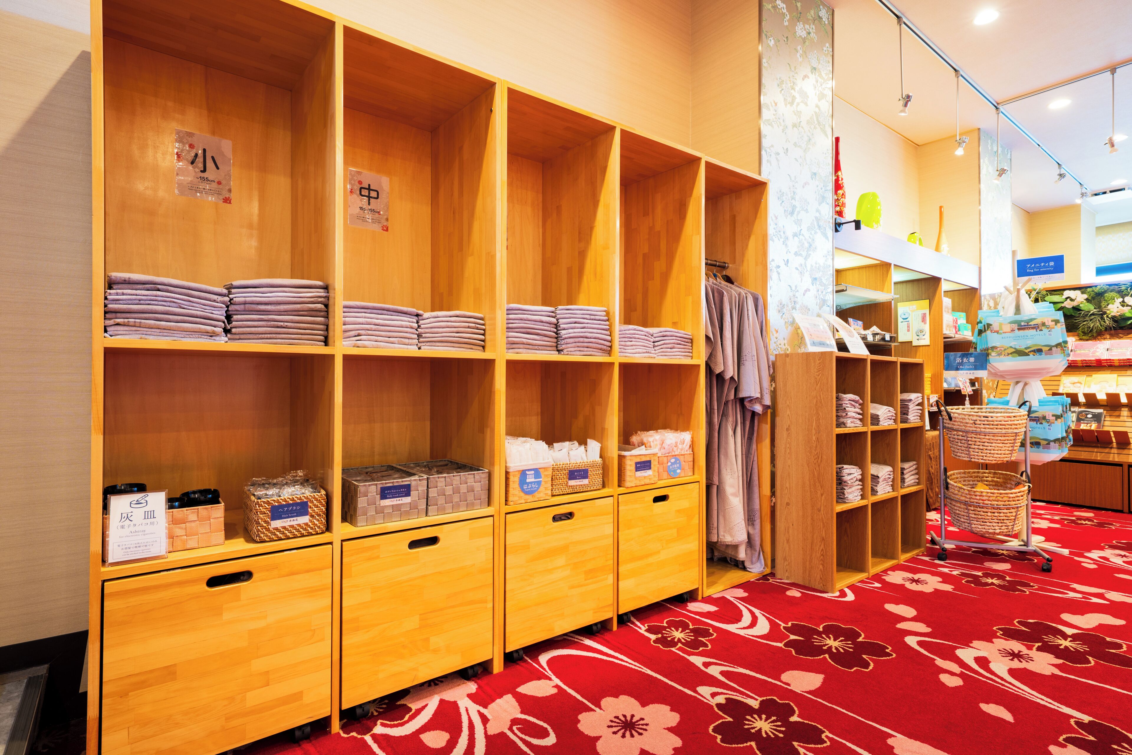 A hotel room with wooden shelving units, neatly folded towels, and a red floral carpet.