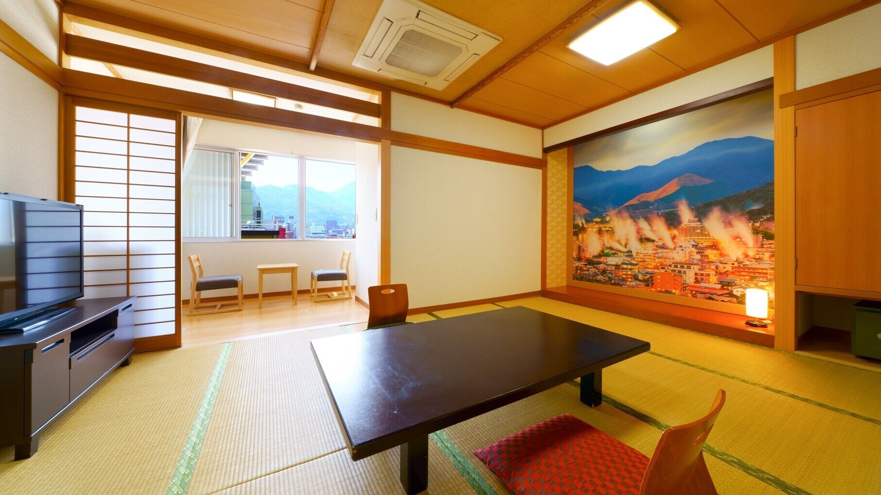 A traditional Japanese room with tatami flooring, a low table, chairs, a television, and a painting of a cityscape.
