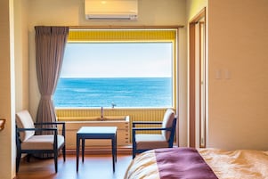 Una habitación con un ventanal grande con vistas al mar, una cama, dos sillas, una mesita y un equipo de aire acondicionado.