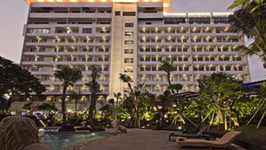 Un hôtel à plusieurs étages doté d’une piscine, entouré de palmiers et de chaises longues.