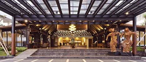 A hotel entrance with a modern design, featuring a glass canopy, a reception desk, and a decorative statue.