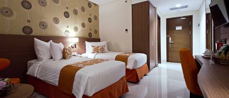 Habitación de hotel con dos camas, cabecero de madera, mesa de comedor y televisor.
