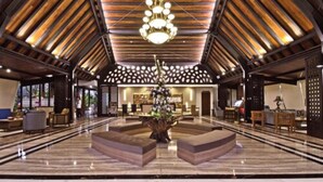 Un hall d’entrée spacieux avec un plafond haut, un lustre central et un coin salon avec des canapés.