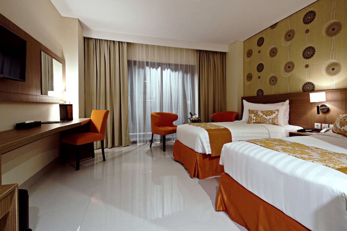 A hotel room with two beds, a desk, a chair, a TV, and a large window with curtains.