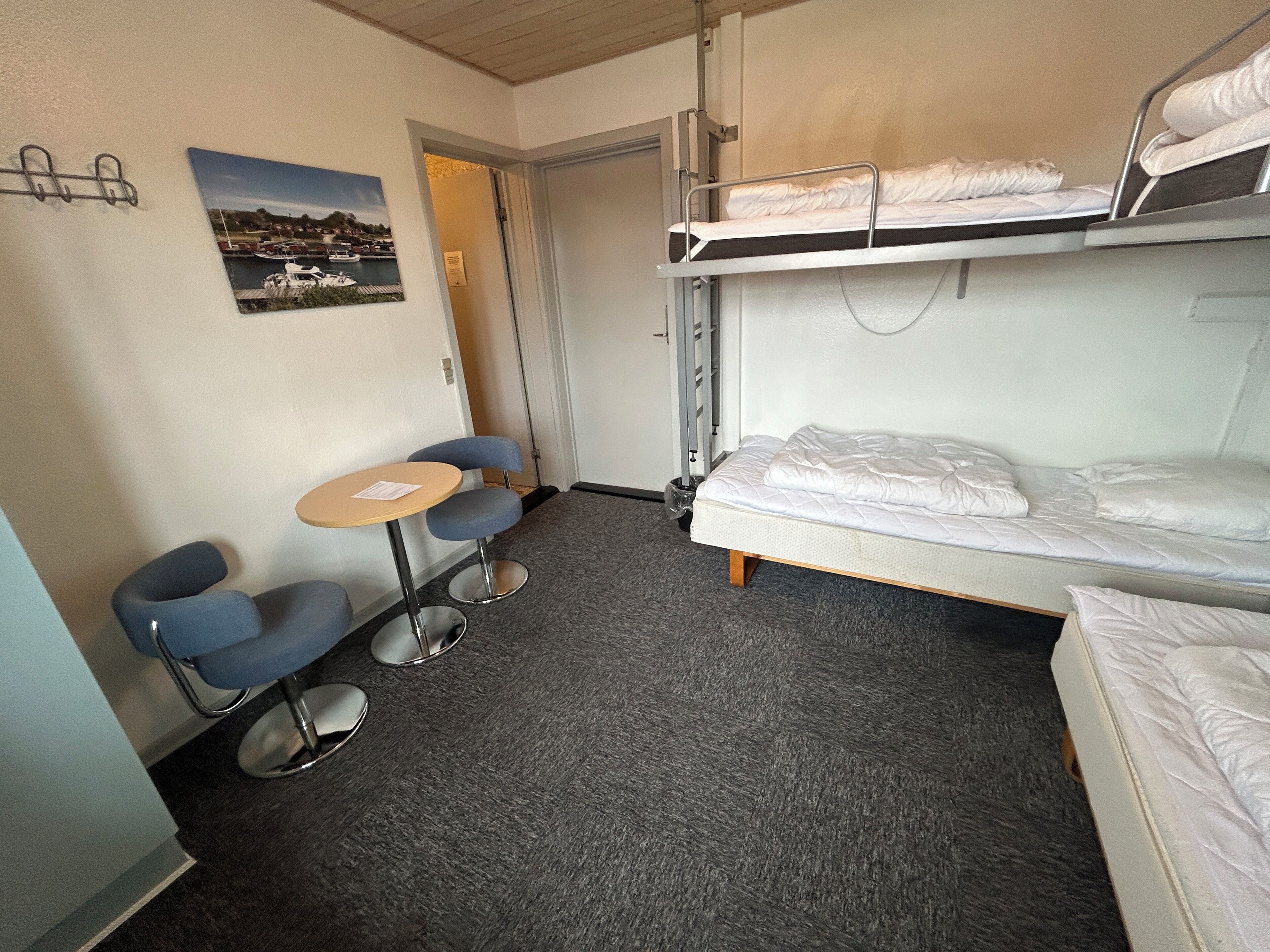 A compact hotel room with bunk beds, a small table, two chairs, and a single bed.