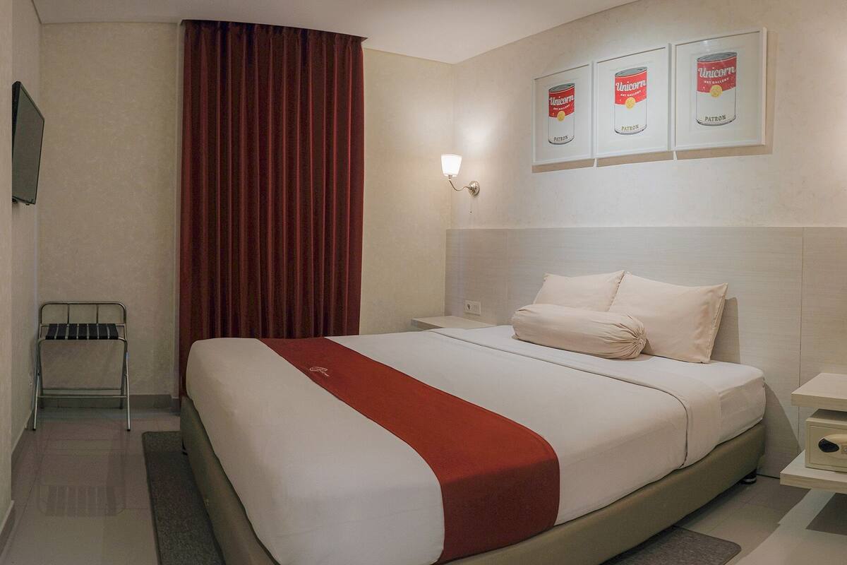 A hotel room with a bed, a nightstand, a lamp, a chair, and a wall with framed pictures.