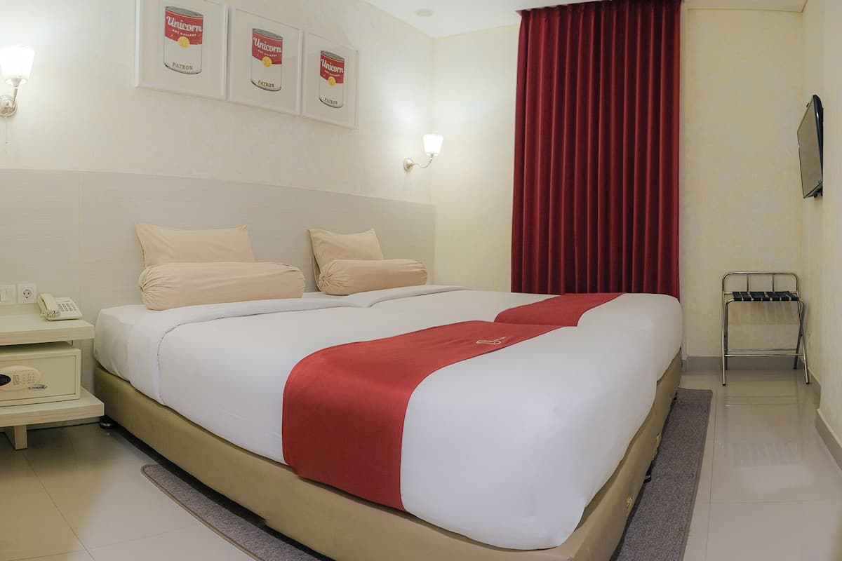 A hotel room with a large bed, a bedside table with a phone, and a red curtain.