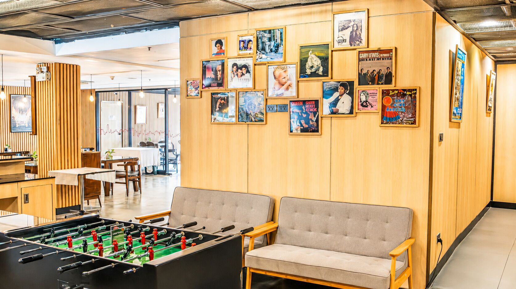 Een kamer met een tafelvoetbaltafel, banken en een muur versierd met verschillende posters.