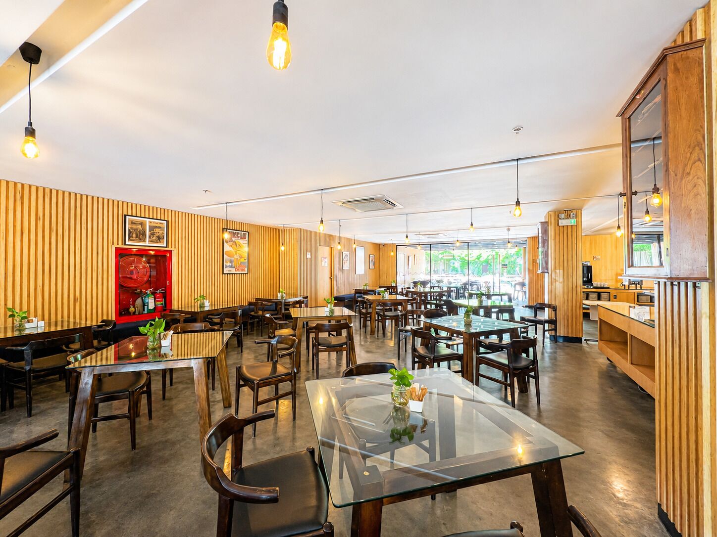 Un restaurante con varias mesas y sillas, paredes de paneles de madera y lámparas colgantes.