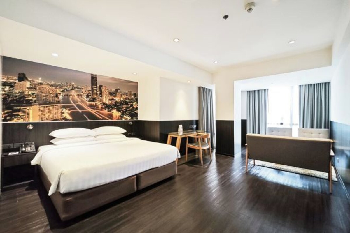 A modern hotel room with a large bed, a seating area, and a cityscape mural on the wall.