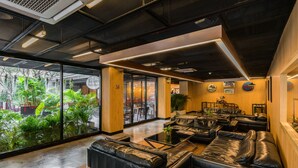 Un espace de détente moderne avec des canapés en cuir, un mur de verre donnant sur un espace verdoyant et un plafond laissant apparaître les conduits.