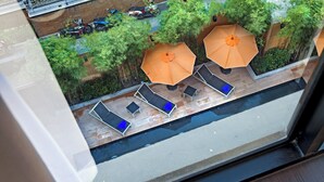 Une terrasse sur le toit, dotée de trois chaises longues et de deux parasols orange, qui offre une vue sur une rue où sont garées des motos et un scooter.