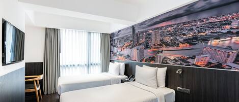 A hotel room with two beds, a desk, a chair, and a large cityscape mural on the wall.