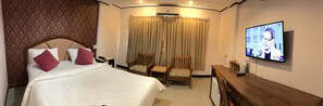 A hotel room with a large bed, two chairs, a TV, and a desk. - At Bangkok Hotel (Bangkok)