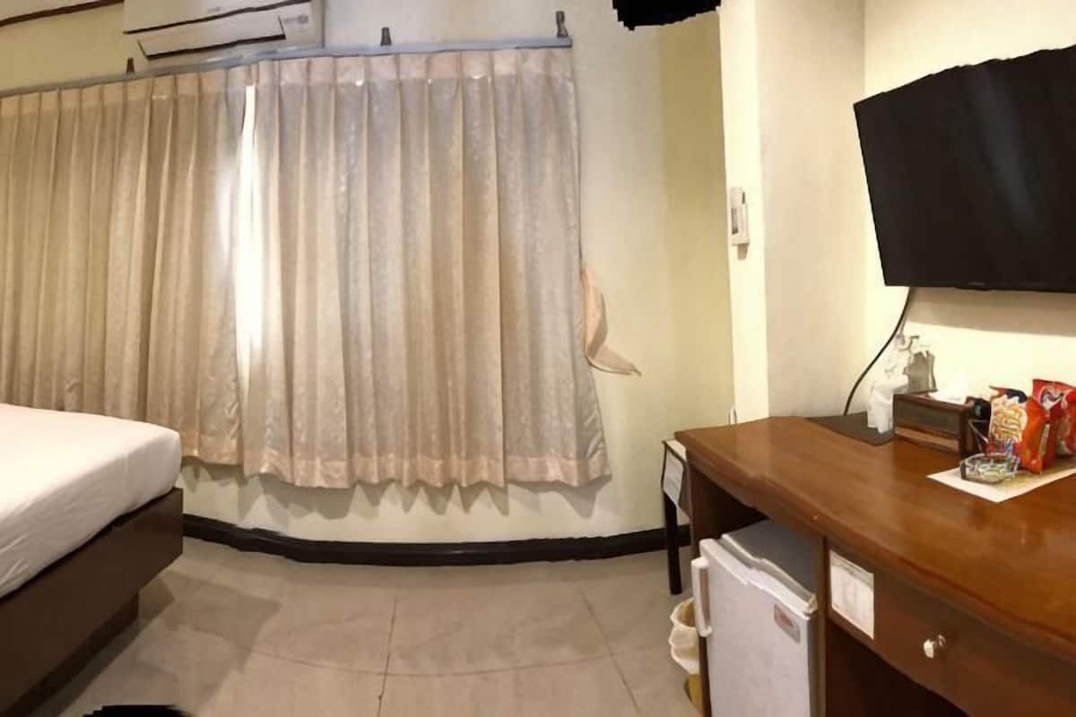 A hotel room with a bed, a wooden desk, a television, and a refrigerator.
