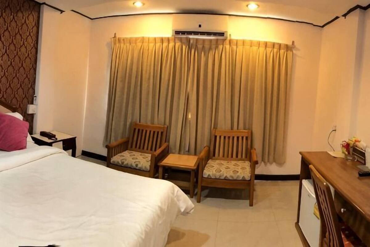 A hotel room with a bed, two chairs, a desk, and a window with curtains.