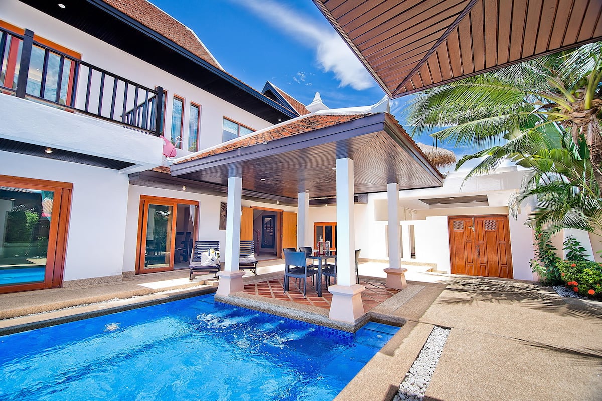Una casa moderna con piscina, un porche cubierto y una puerta de madera.