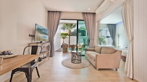 A modern living room with a dining area, a sofa, a TV, and a view of a balcony with plants. - Tropicana Pool Villa (Pattaya)