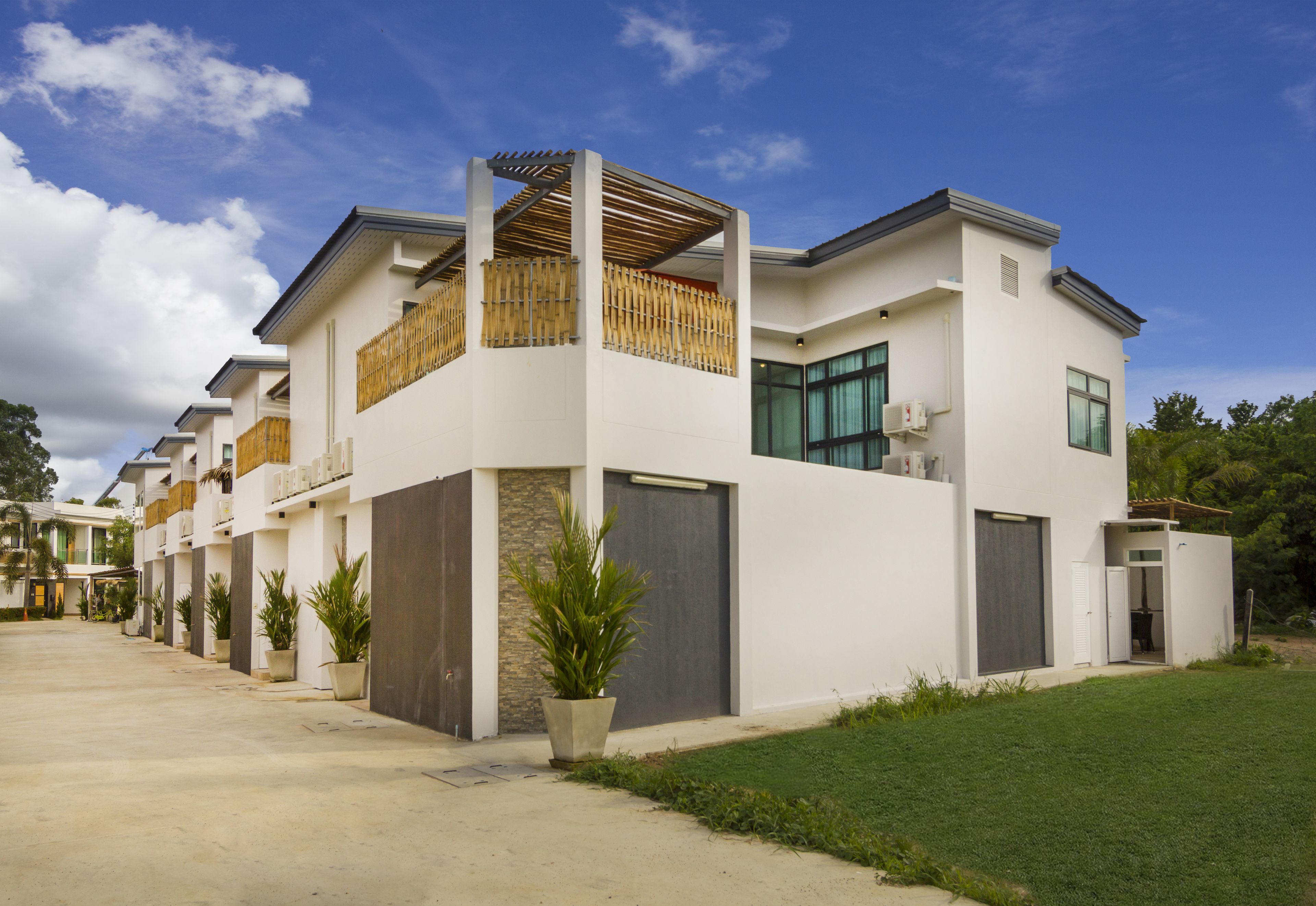 A modern multi-story residential building with a covered balcony, large windows, and a well-maintained lawn.