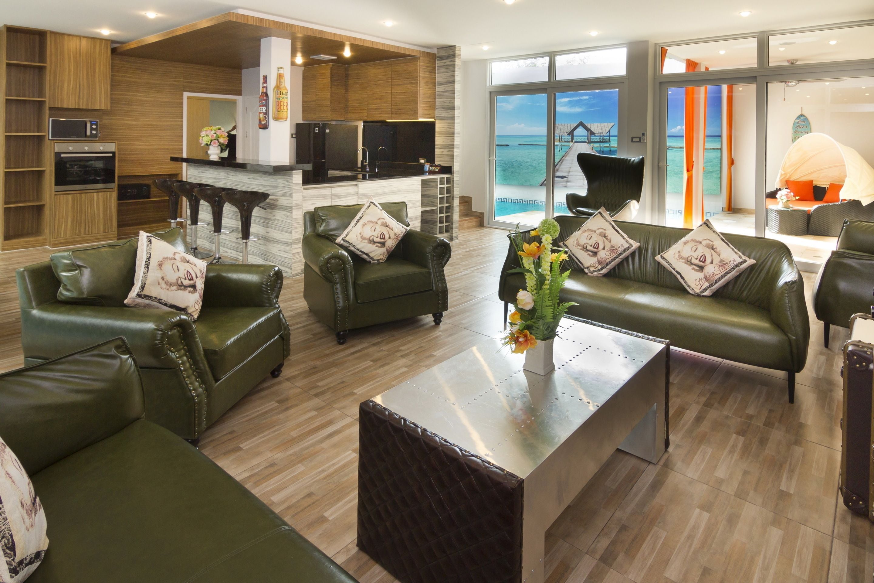 A modern living room with green leather sofas, a coffee table, and a kitchen area with a bar.