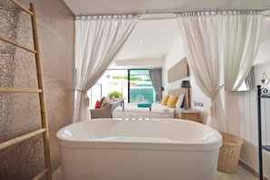 Casa de banho moderna com uma banheira grande, uma escada de madeira e vista para uma piscina através das cortinas.