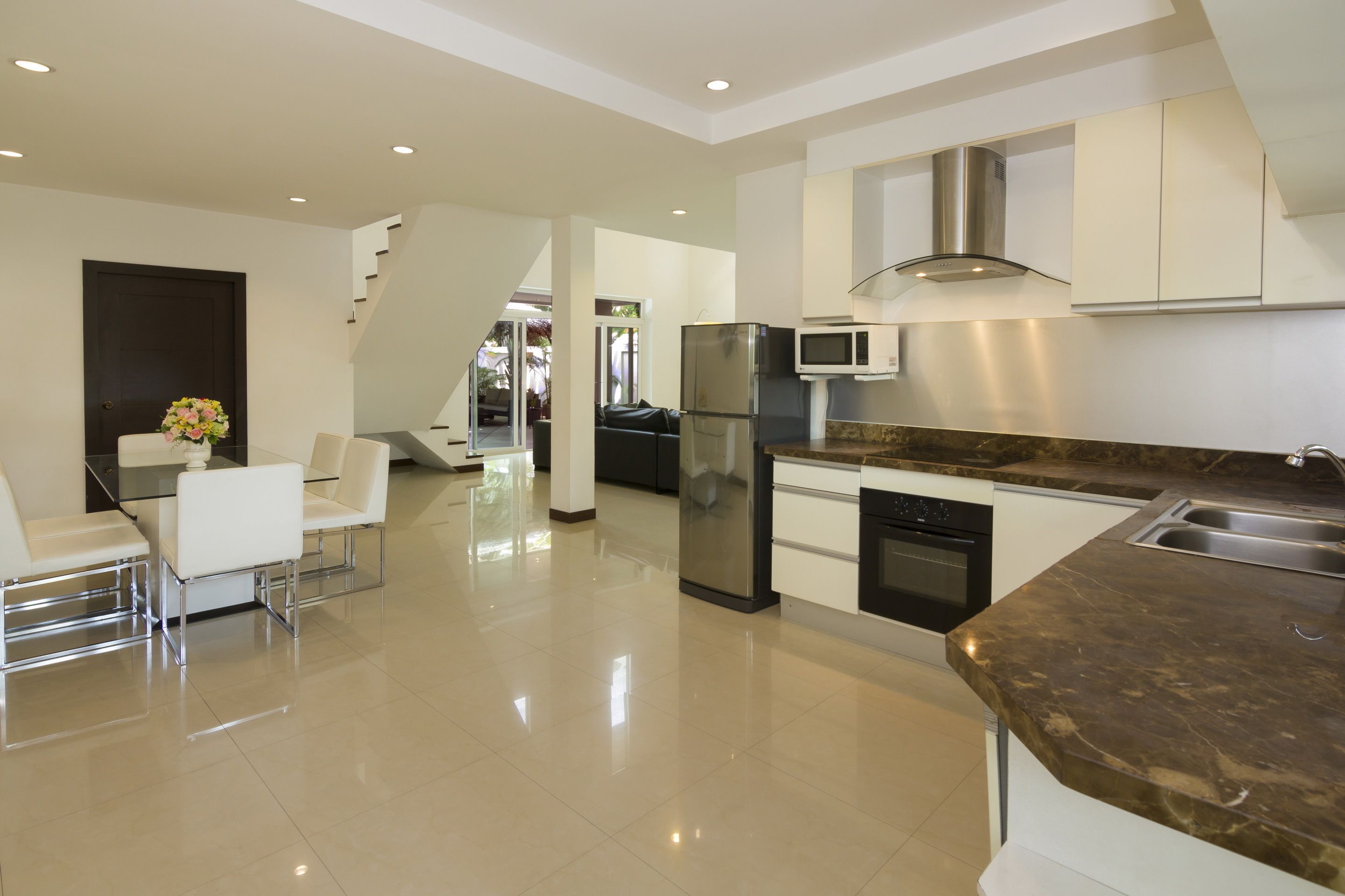 Una cocina moderna con encimera de mármol, electrodomésticos de acero inoxidable y un comedor con sillas blancas.