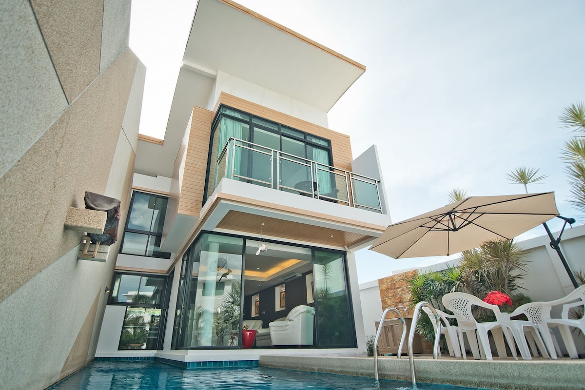 Una casa moderna de dos pisos con un balcón acristalado, una piscina y mobiliario de exterior.