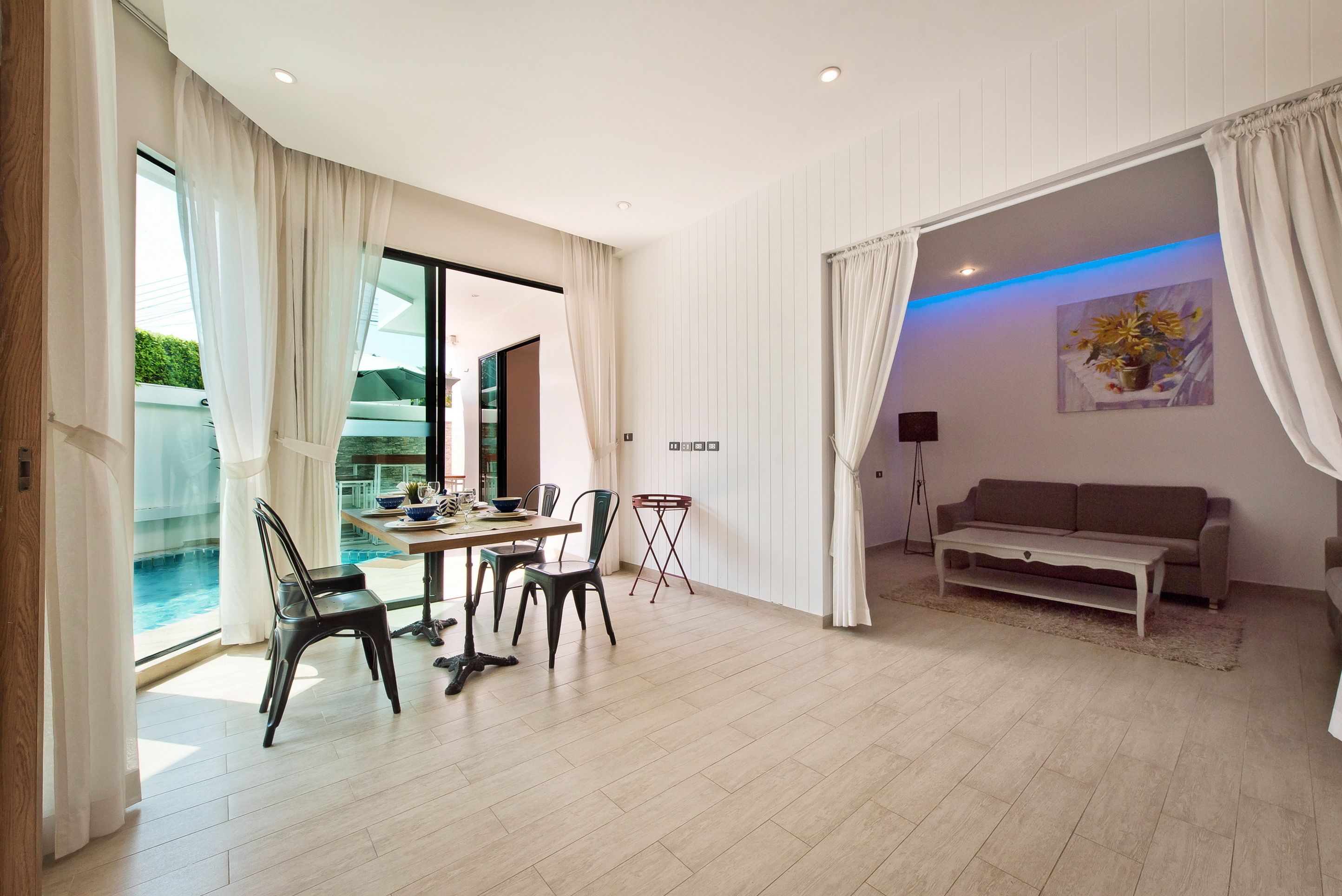 Un vaste espace de vie comprenant une table à manger, des chaises, un canapé et une grande fenêtre donnant sur une piscine.