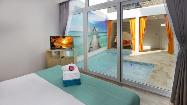 A hotel room with a bed, a TV, a view of a pool and a deck, and a large sliding glass door. - Tropicana Pool Villa (Pattaya)