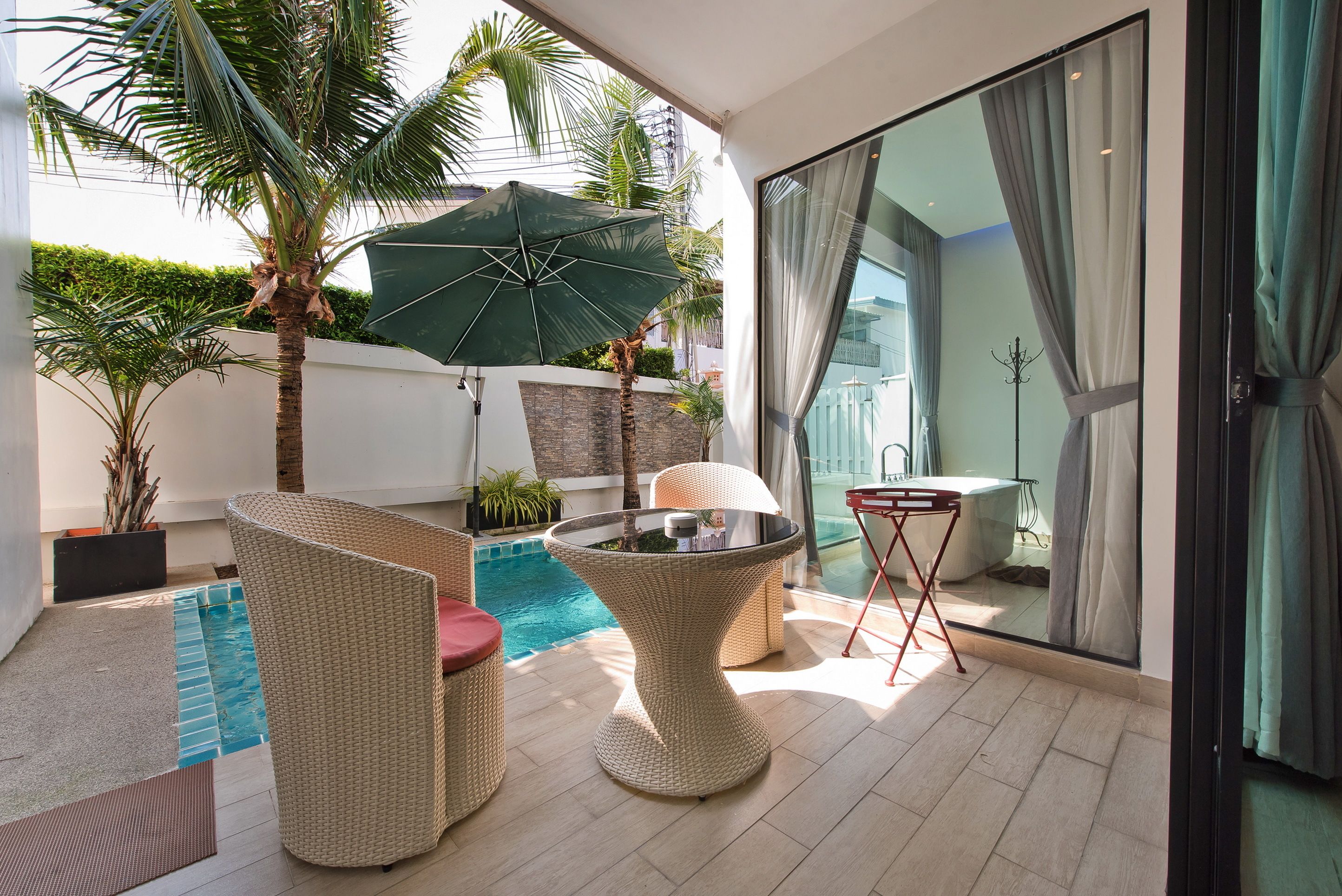 Une terrasse extérieure moderne, dotée de meubles en osier, d’une piscine et d’une porte vitrée donnant sur un balcon.