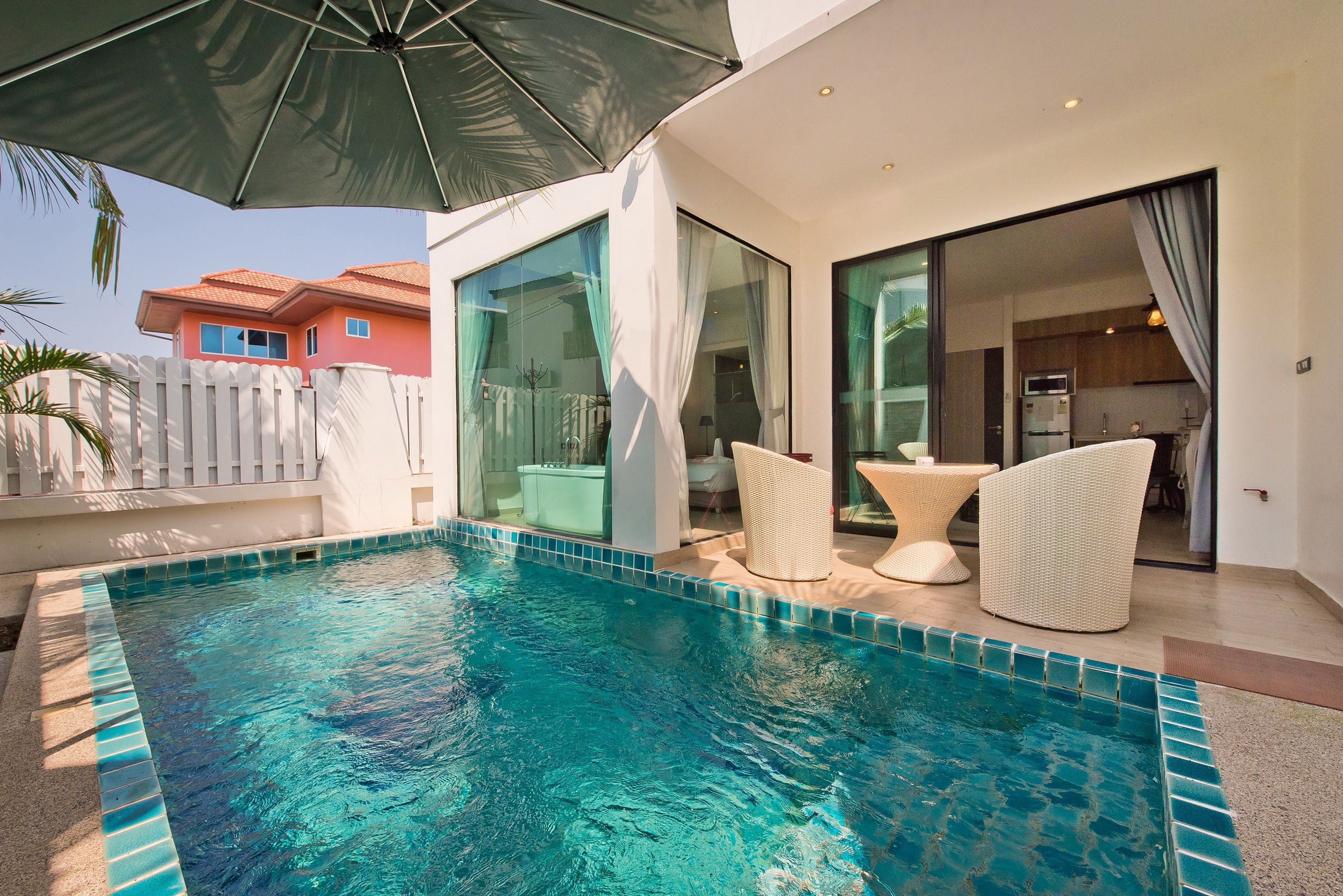 A modern outdoor pool area with a glass-enclosed patio, wicker furniture, and a view of the adjacent building.
