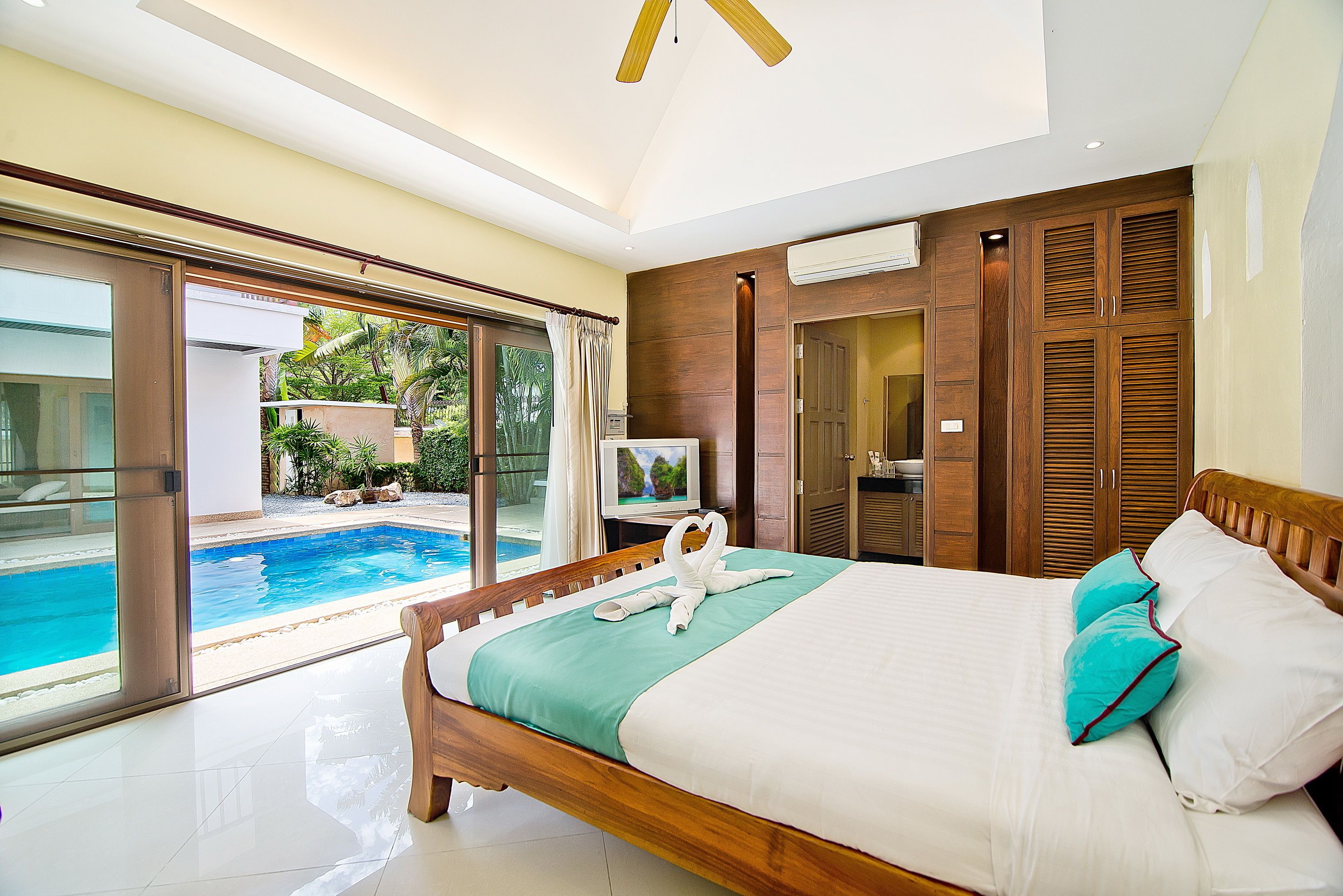 A bedroom with a large bed, a TV, and a view of a swimming pool.