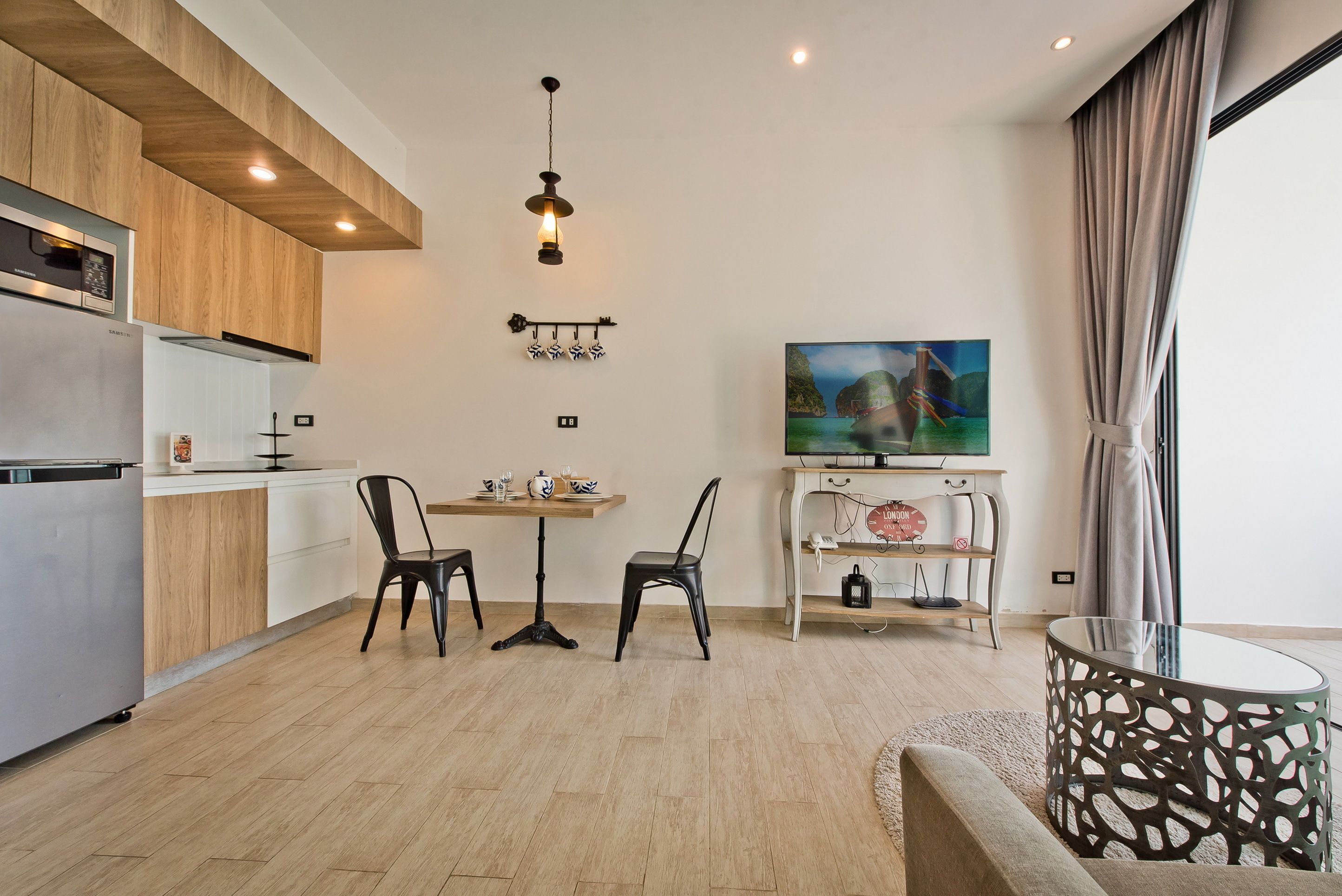 A modern kitchen with wooden cabinets, a dining area with two chairs, a table, and a TV on a stand.