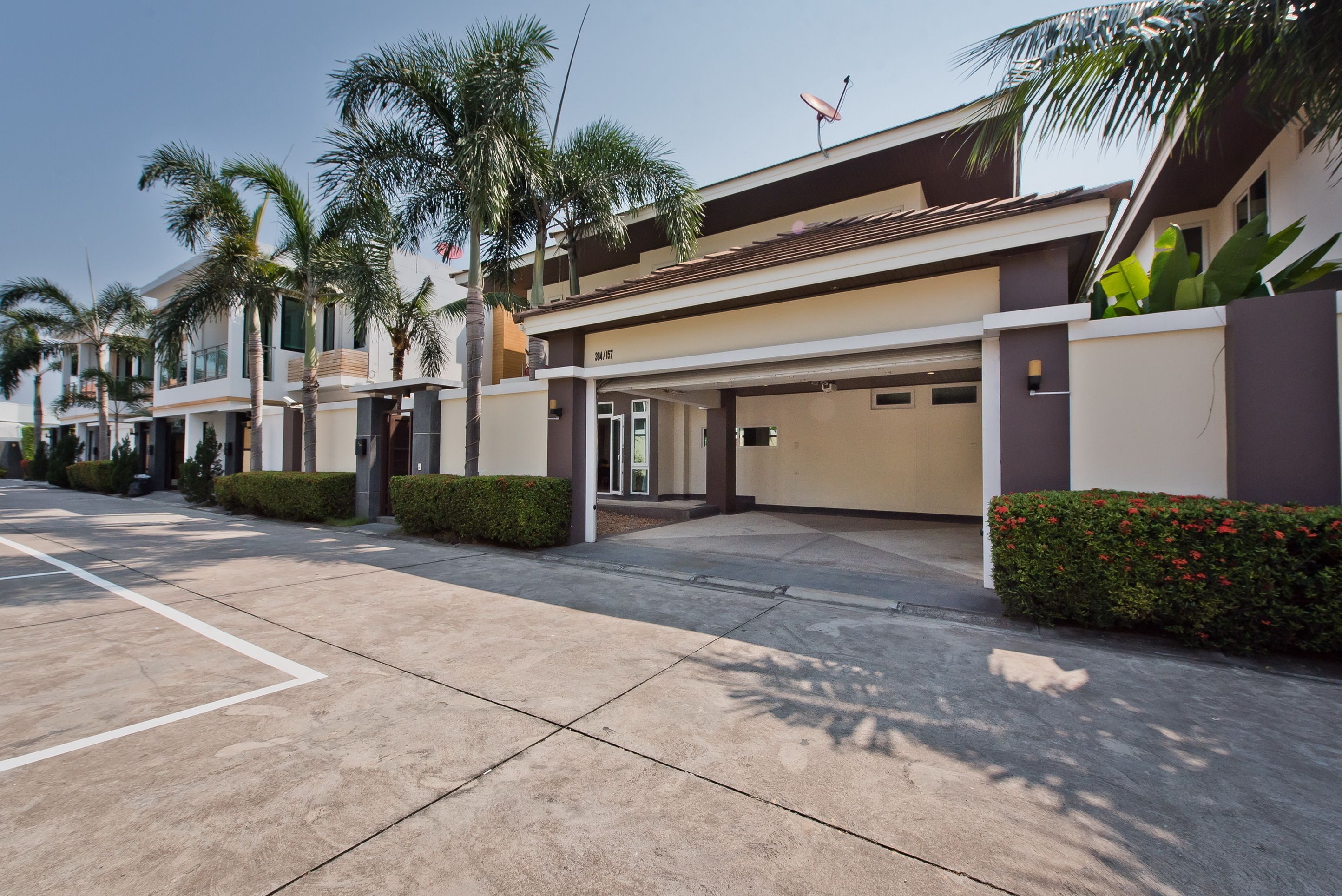 A modern residential building with a covered driveway, palm trees, and a satellite dish.