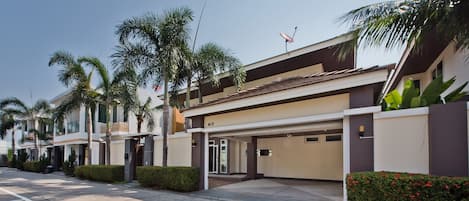A modern residential building with a covered driveway, palm trees, and a satellite dish.