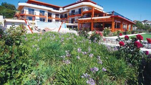 A modern hotel with a multi-story structure, outdoor seating area, and a well-maintained garden with flowers. - Alacati Villa Renk (Cesme)
