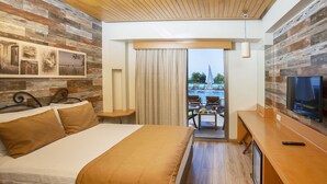 A hotel room with a bed, a TV, a wooden ceiling, and a view of an outdoor pool area. - Alacati Villa Renk (Cesme)