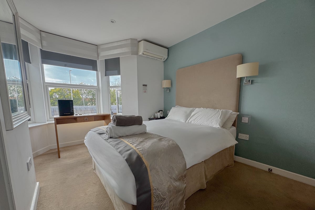 A hotel room with a large bed, a desk with a computer, a window with a view, and an air conditioning unit.