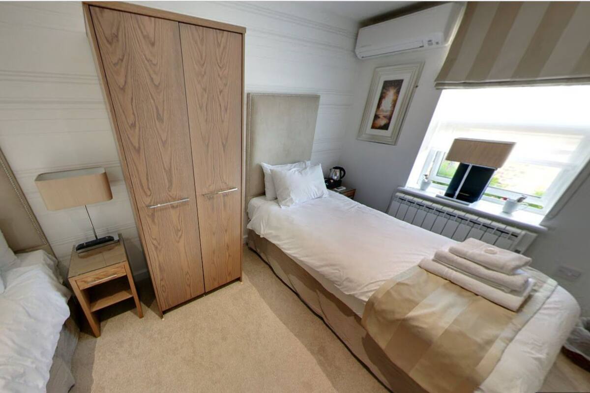 A bedroom with a bed, a wardrobe, a bedside table, a lamp, a radiator, and a window with a view.
