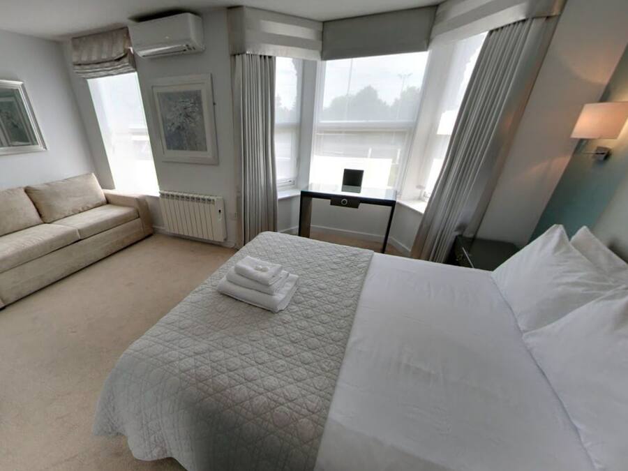A hotel room with a bed, a sofa, a desk, and a window with curtains.