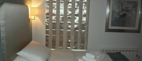 A neatly made bed with white linens, a wall-mounted lamp, and a framed artwork on the wall.