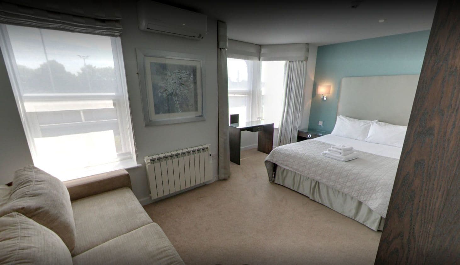 A hotel room with a large bed, a sitting area with a sofa, a desk, and a window with curtains.