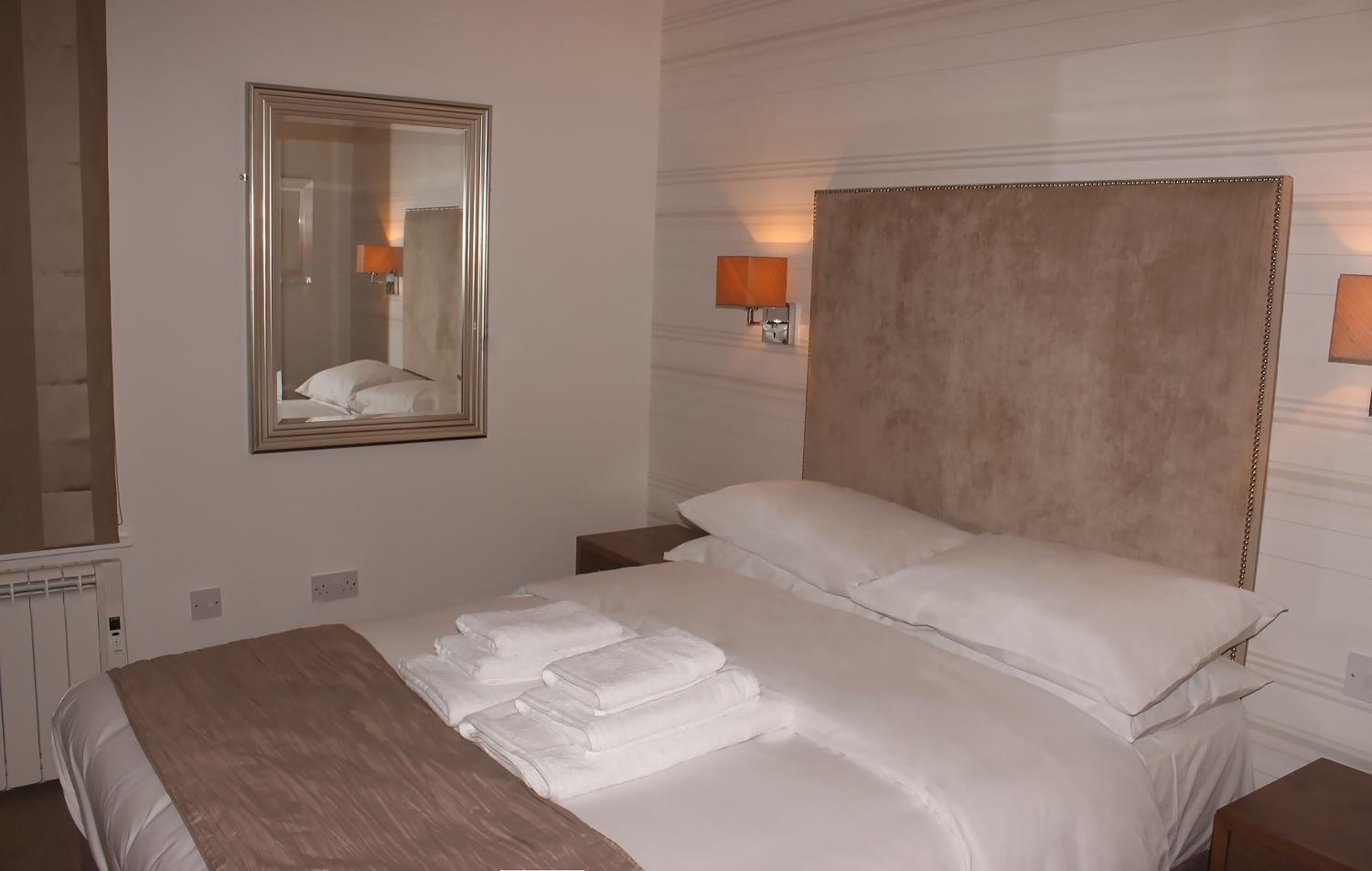 Ein Hotelzimmer mit einem großen Bett, einem Kopfteil, einem Spiegel und zwei Wandlampen.